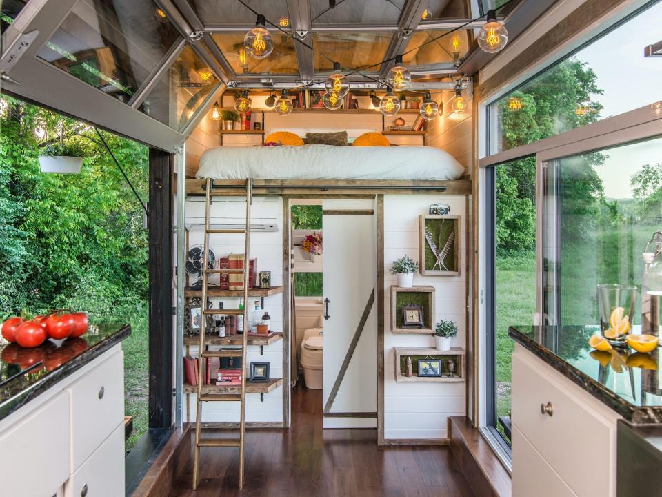 a lofted bed over a bathroom behind a kitchen