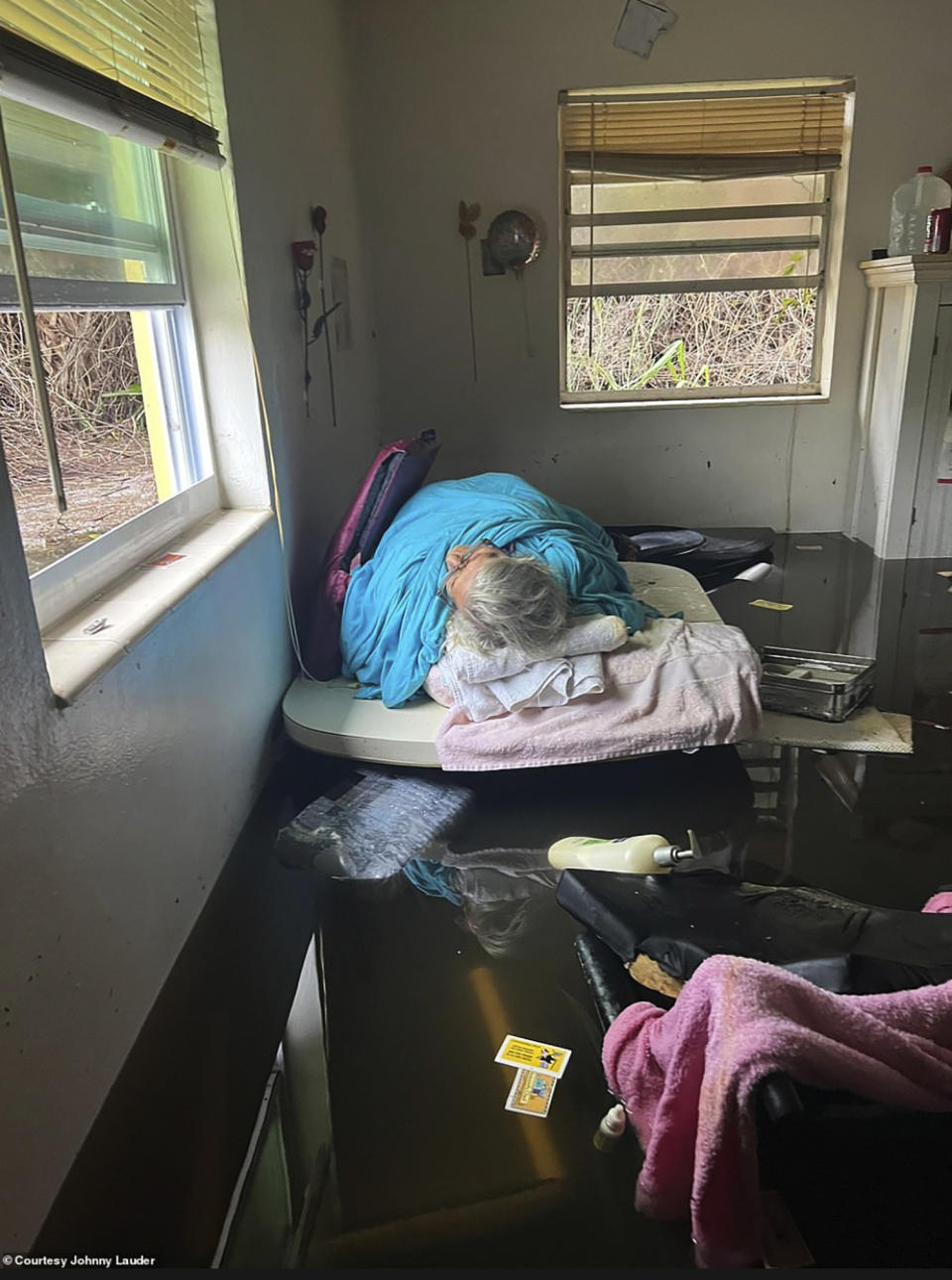 In this photo provided by Johnny Lauder, Lauder's mother, Karen Lauder, 86, lies just above the water line on a table, wrapped in sheets to keep warm after water flooded her home, in Naples, Fla., Wednesday, Sept. 28, 2022, following Hurricane Ian. (Johnny Lauder via AP)