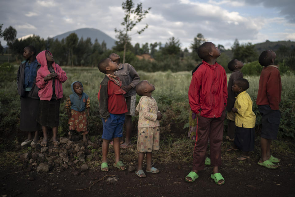 In this Sept. 7, 2019 photo, children watch a drone flying near the Volcanoes National Park in Kinigi, Rwanda. In 2005, the government adopted a model to steer 5% of tourism revenue from Volcanoes National Park to build infrastructure in surrounding villages, including schools and health clinics. Two years ago, the share was raised to 10%. (AP Photo/Felipe Dana)