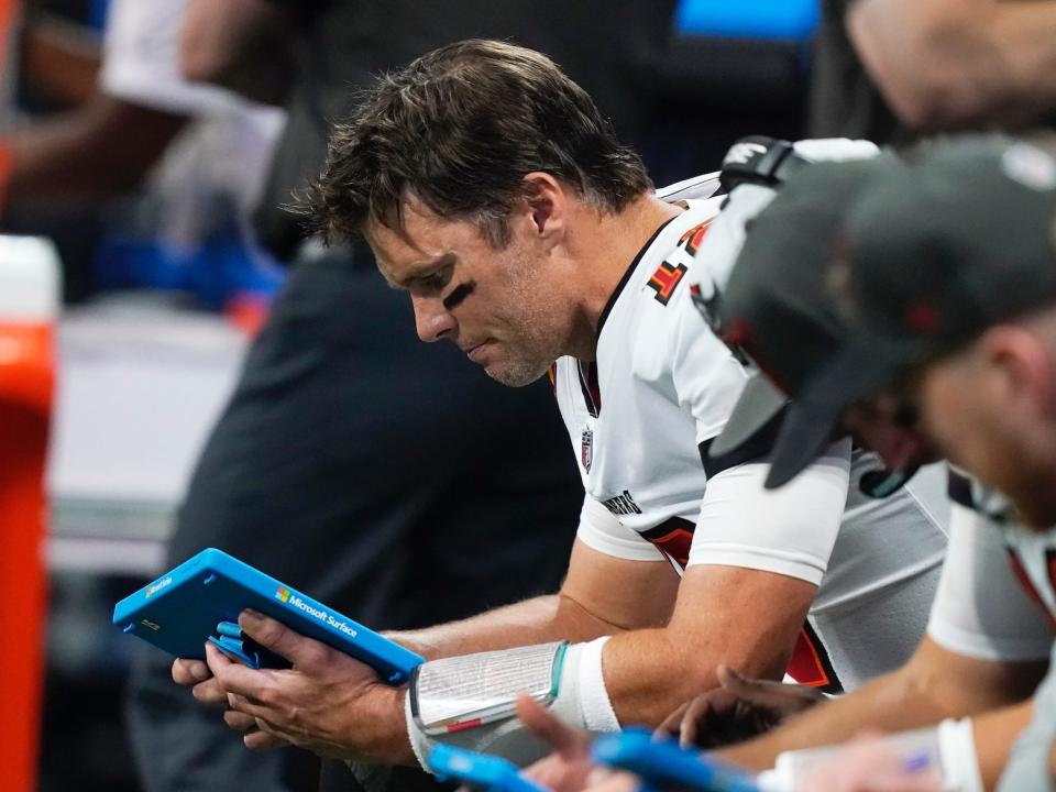 Tom Brady sits on the bench and looks at a tablet in 2021.
