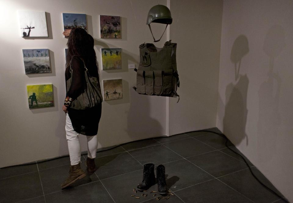 In this photo taken Saturday, May 10, 2014, a woman looks at acrylic on canvas paintings by Palestinian artist Shareef Sarhan named Remains of a Battle, during an art exhibition "Traces, a testimony to memory," displaying over forty Palestinian artists work from Gaza, in the West Bank city of Ramallah. The Gaza Strip is tough turf for artists. An Israeli-Egyptian border blockade of the Hamas-ruled territory keeps them away from an international audience and potential buyers, while the local art market is close to nil. A new exhibit now offers them a chance to showcase their work outside Gaza. (AP Photo/Nasser Nasser)