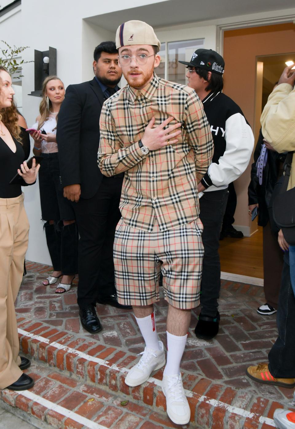 Angus in a matching plaid button-down top and shorts with a backwards kangaroo hat and tall white socks and sneakers.