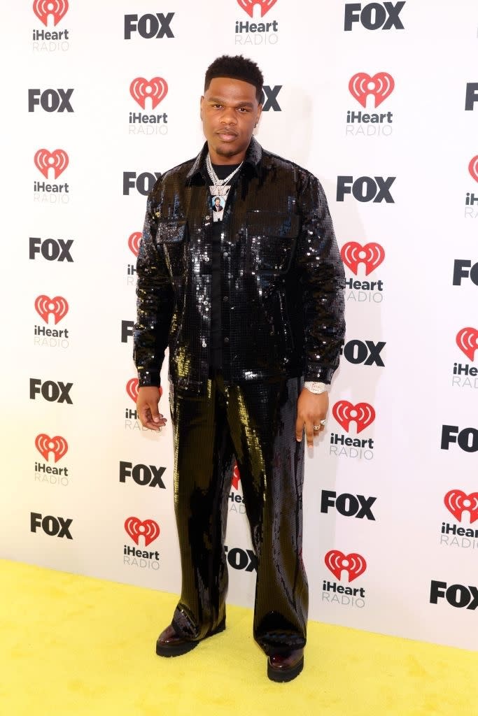Man in glittering black suit standing on the yellow carpet at iHeartRadio event