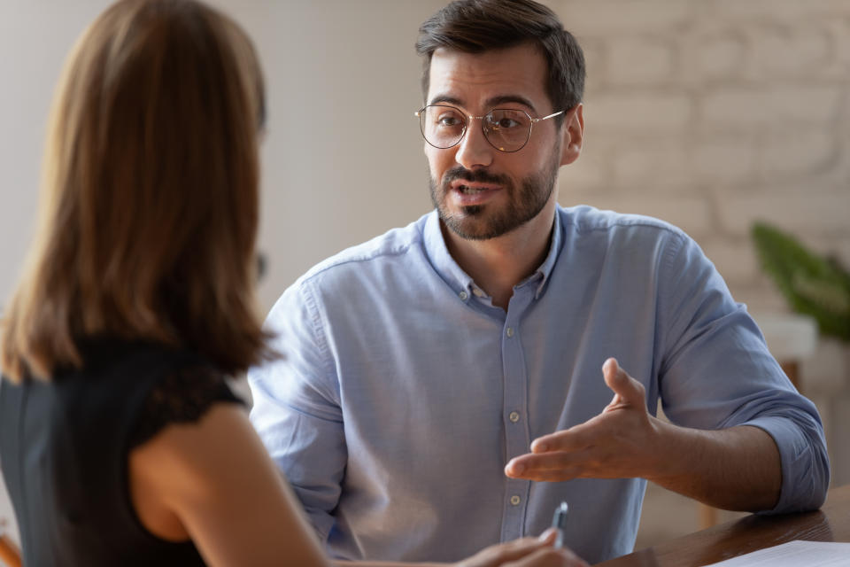 A man gestures while speaking to a woman in what appears to be an interview setting.