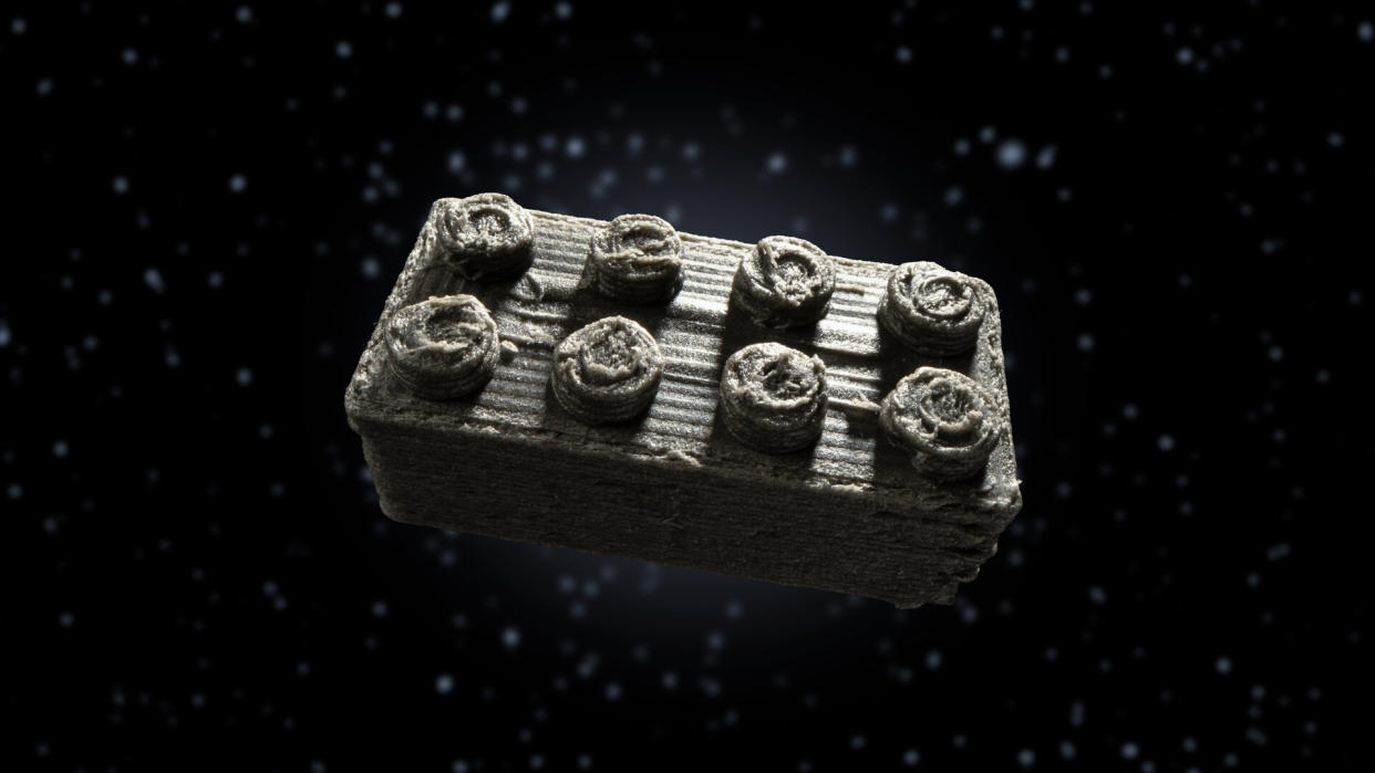  A roughly sculpted grey lego brick floats in space. 