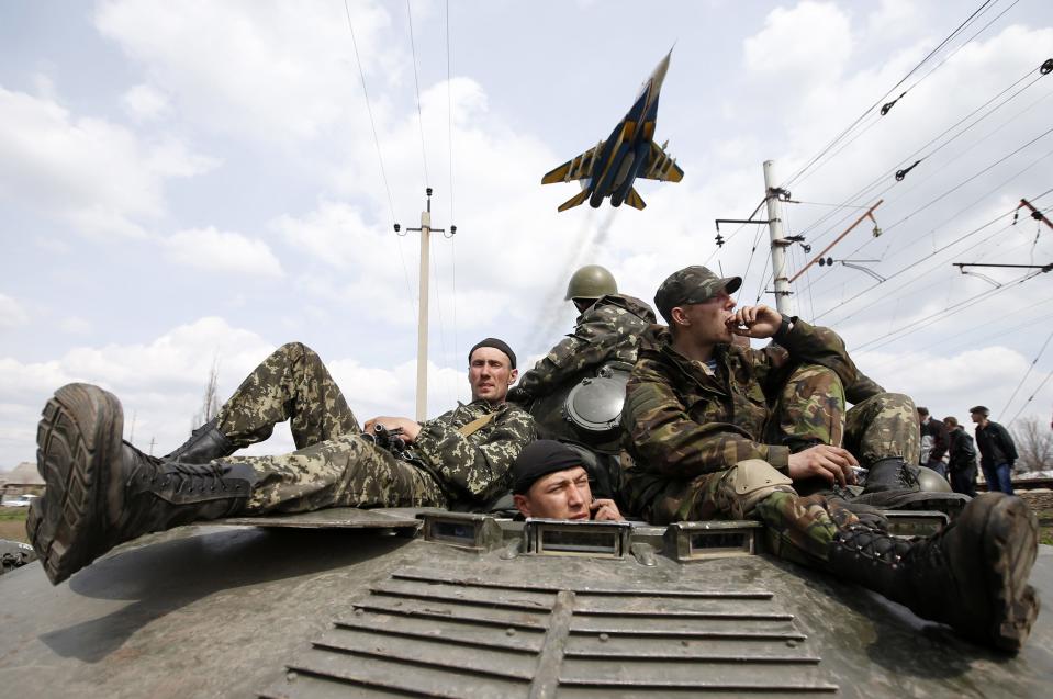 A fighter jet flies above as Ukrainian soldiers sit on an armoured personnel carrier in Kramatorsk