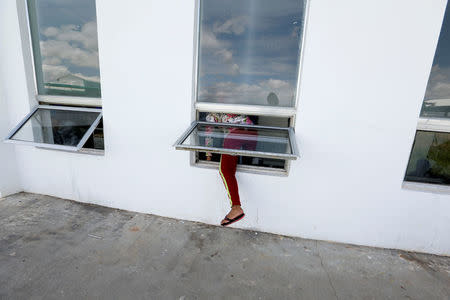 A worker climbs through the window to go back to work after an hour lunch break at Complete Honour Footwear Industrial, a footwear factory owned by a Taiwan company, in Kampong Speu, Cambodia, July 4, 2018. REUTERS/Ann Wang