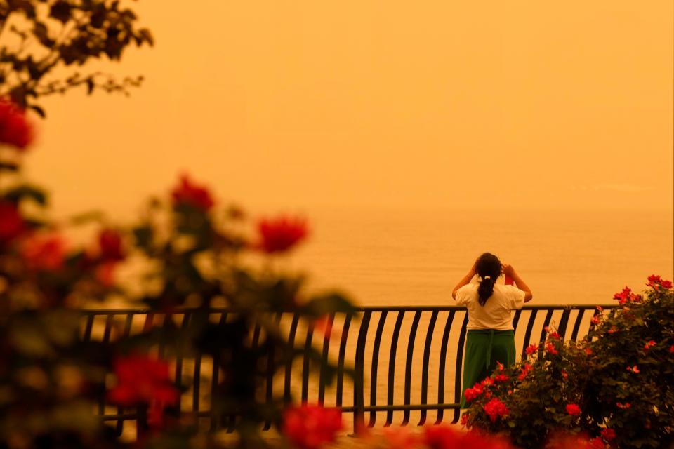 A woman pauses at the Hudson River to take pictures as the sky changed colors due to the Canadian wildfires. Wednesday, June 7, 2023 