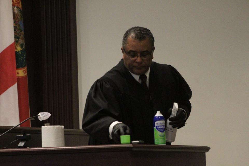 Circuit Judge Raul Zambrano disinfects the witness stand after a Florida Department of Law Enforcement analyst, who wore a mask and said she was sick but did not have COVID, testified on Friday during the trial of Noah Motto.