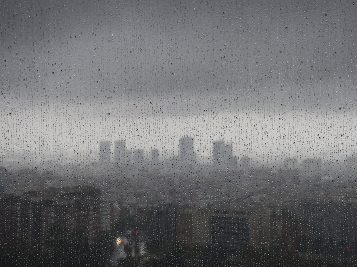 After heavy rainfall, the diffuse skyline of Barcelona is emerging in the twilight behind raindrops on a window.