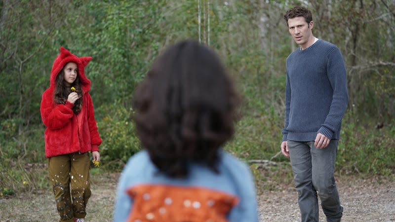 Two children, one with their back to the camera, stare at an uneasy-looking man.