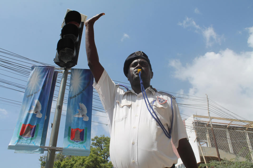 In this photo taken,Wednesday, Dec, 4, 2013. A Somali traffic police man raises his hand and stands near a street signal to try and stop cars as the traffic light flashes red. Mogadishu in recent months has started to install road signs for the first time after decades of lawlessness left a culture of “anything goes” on the road. Large parts of the country's residents are unfamiliar with traffic laws, increasing the pressure on traffic police struggling to impose law and order in a dangerous and chaotic city. (AP Photo/Farah Abdi Warsameh)