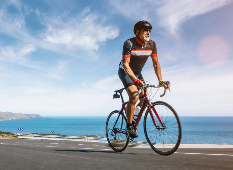 hombre maduro montando en bicicleta corriendo a lo largo de la costa, ejerciendo hábitos que retrasan el envejecimiento