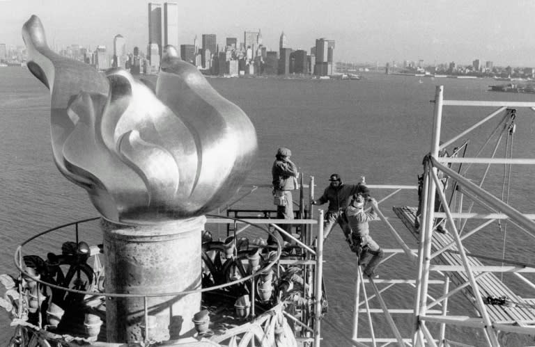 Workers remove scaffolding from around the torch of the Statue of Liberty, one of the world's most famous landmarks, with Manhattan skyline and the twin towers of the World Trade Center seen in the background, in 1985