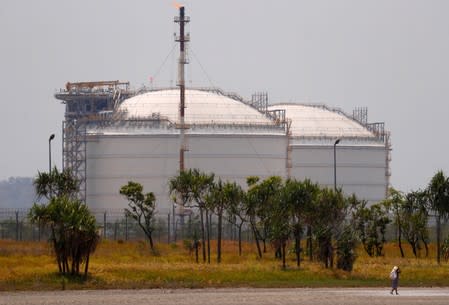 A woman carrying a bag containing firewood walks in front of two Liquefied Natural Gas (LNG) storage tanks at the ExxonMobil PNG Limited-operated LNG plant at Caution Bay, located on the outskirts of Port Moresby