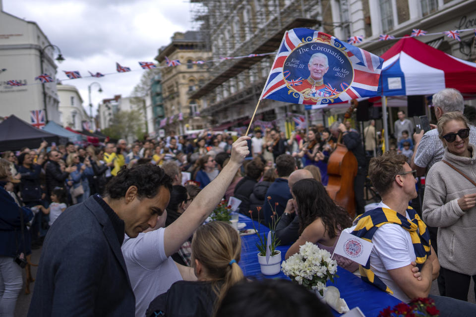 Musicians play their instruments as people sit at long tables to eat their lunch as part of the Big Lunch celebration in London, Sunday, May 7, 2023. The Big Lunch is part of the weekend of celebrations for the Coronation of King Charles III. (AP Photo/Emilio Morenatti)