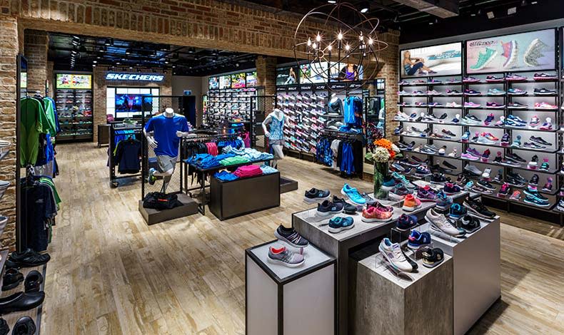 The interior of a Skechers retail store. Shoes and other sports apparel is displayed on shelves and on boxes in the middle of the floor.