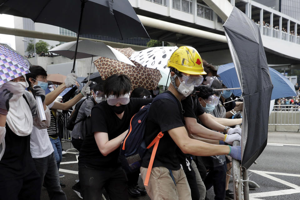 In this photo taken on Wednesday, June 12, 2019, protesters wear protection gears and use umbrellas to shield themselves as they gather near the Legislative Council in Hong Kong. Young Hong Kong residents protesting a proposed extradition law that would allow suspects to be sent to China for trial are seeking to safeguard their identities from potential retaliation by authorities employing mass data collection and sophisticated facial recognition technology. (AP Photo/Kin Cheung)