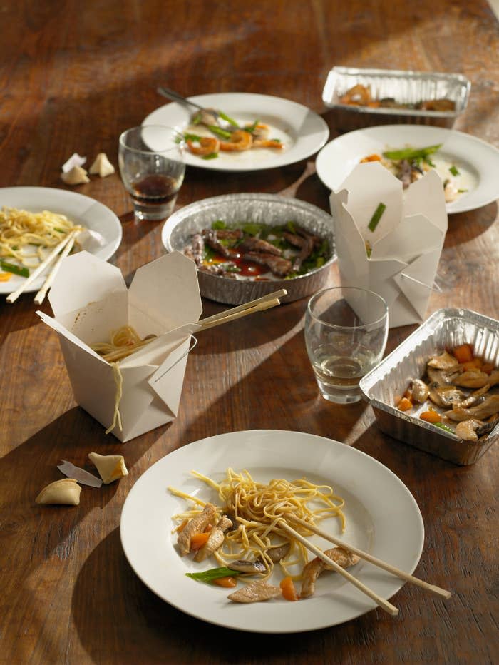 Assorted Chinese takeout containers with leftovers on a wooden table