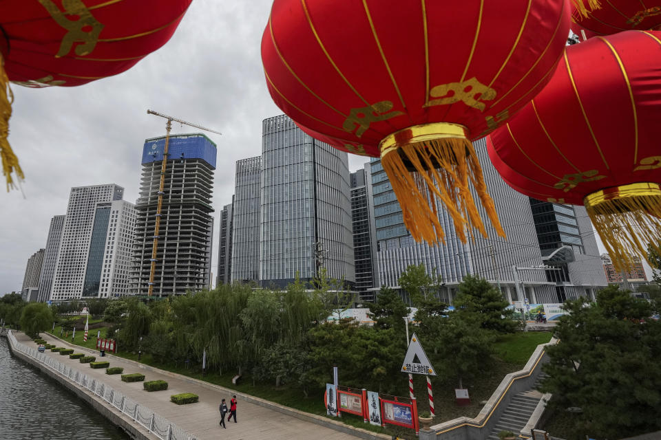 People walk along a riverbank near a commercial office buildings under construction in Tongzhou, outskirts of Beijing, Monday, Oct. 4, 2021. China’s economy is losing steam as President Xi Jinping's government cracks down on corporate debt and energy use in pursuit of more stable, sustainable growth. (AP Photo/Andy Wong)