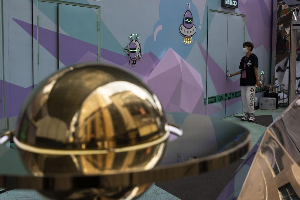 A worker wearing a mask to protect against the coronavirus walks past space themed displays promoting an online service in Beijing, China on Monday, Aug. 3, 2020. An outbreak in China's far northwestern region of Xinjiang is continuing to subside. (AP Photo/Ng Han Guan)