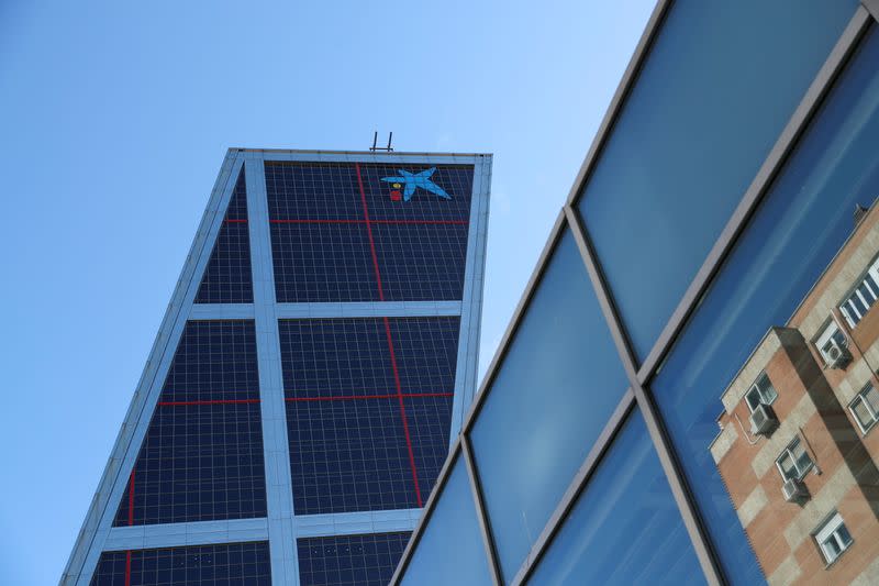 A building is reflected on glass next to CaixaBank headquarters in Madrid