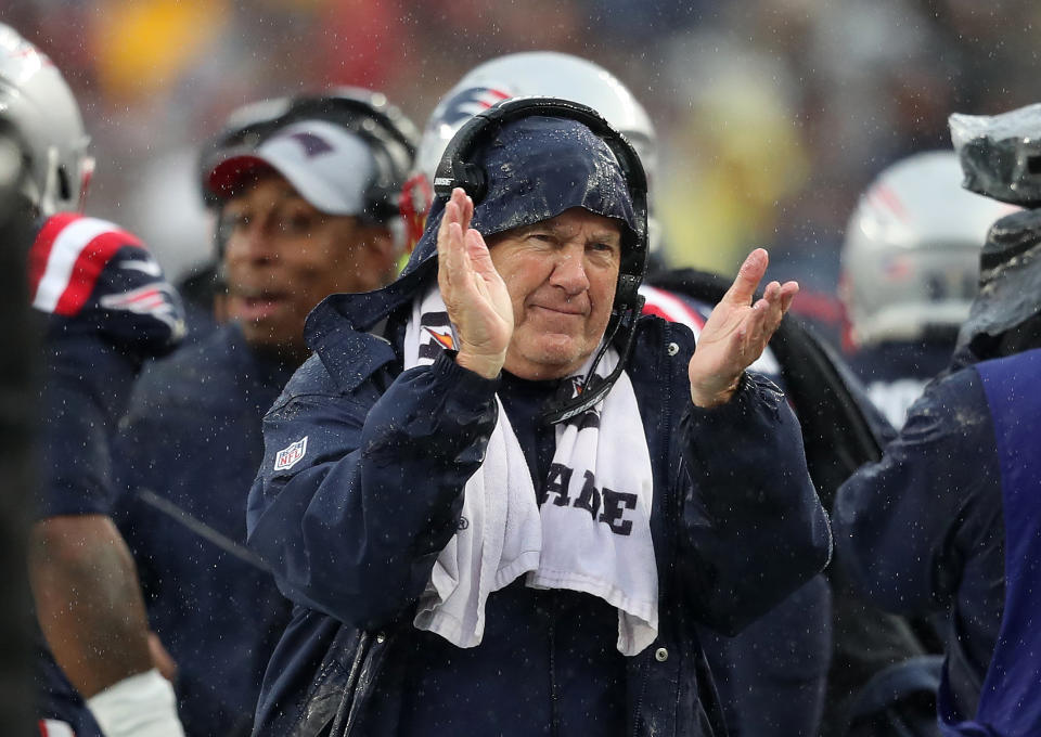 Bill Belichick claps while wearing a hoodie during a game.