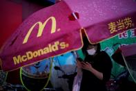 Woman wearing a face mask checks her mobile phone under an umbrella with a McDonald's sign in Xianning