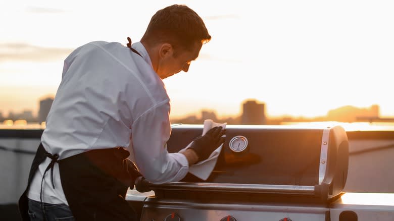 A person cleaning a grills exterior at sunset