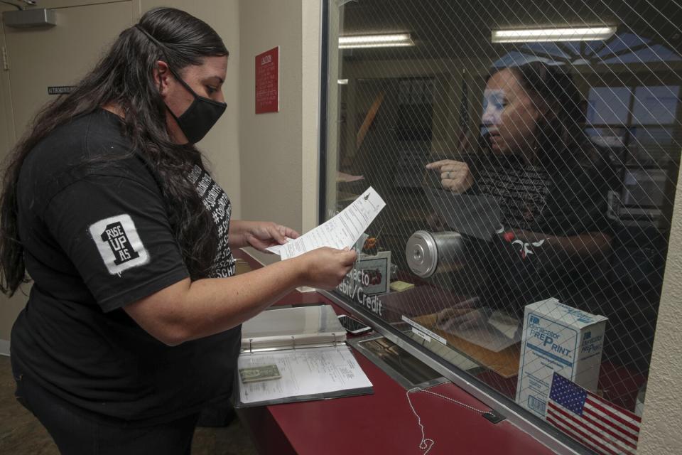 A woman speaks through a glass partition to another woman