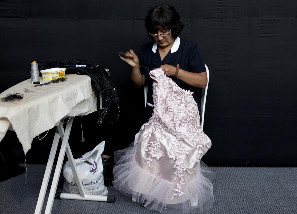 In this April 10, 2013 photo, a seamstress adjusts a dress prior to a show by Peru's designer Claudia Jimenez during Lima Fashion Week in Lima, Peru. The shows are highlighting the work of 16 Peruvian designers of clothes, jewelry and accessories as well as the collection of Spanish designer Agatha Ruiz de la Prada, who was invited as a special participant. (AP Photo/Martin Mejia)