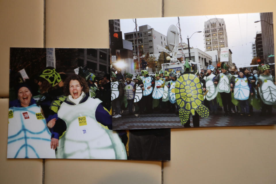 In this photo taken Monday, Nov. 25, 2019, photos on the kitchen table of Lisa Wathne, second left, show her marching with her friend Karen Baker while dressed in sea turtle costumes alongside a wider view of demonstrators during the World Trade Organization (WTO) protests in Seattle 20 years earlier, in Lake Forest Park, Wash. Wathne and other demonstrators wore the cardboard turtle shells to protest WTO policies, including one interpreted by protesters as disregarding the plight of turtles killed by shrimp nets. A wide array of issues brought tens of thousands of protesters to Seattle 20 years ago Saturday, with one unifying theme: concern that the World Trade Organization, a then-little-known body charged with regulating international trade, threatened them all. (AP Photo/Elaine Thompson)