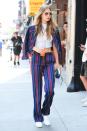 <p>Gigi steps out in multi-colored pinstripe separates with a white mock neck crop top, white sneakers, aviator sunglasses and a colorblocked clutch.</p>