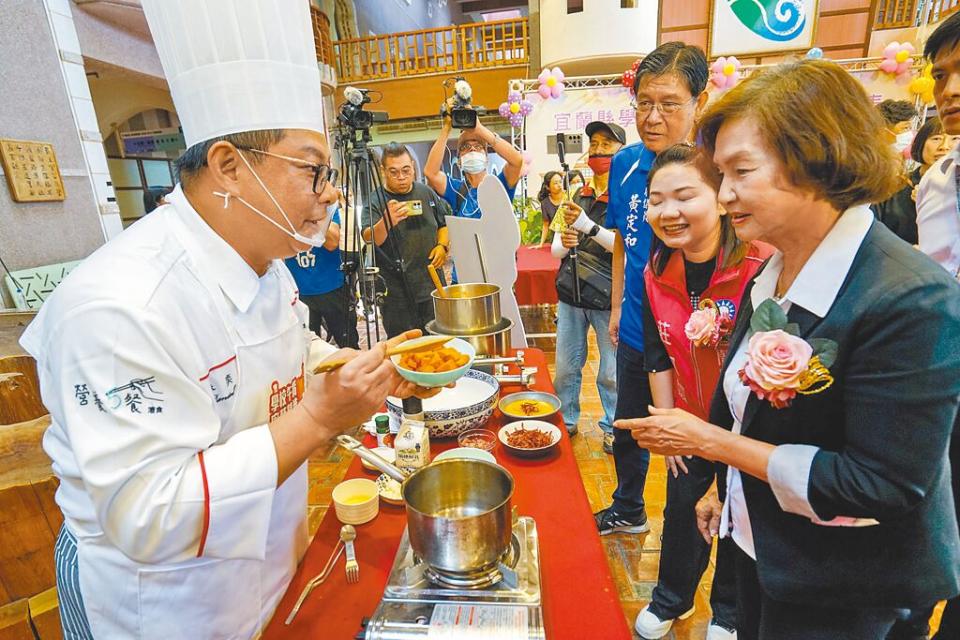 宜蘭縣政府19日舉辦學校午餐廚藝精進成果發表會，灃食公益飲食文化教育基金會顧問主廚林奕成（左）向縣長林姿妙（右）說明「赤珊瑚鴨賞濃湯」的烹調步驟，讓學童品嘗後都不知道湯裡有紅蘿蔔。（李忠一攝）