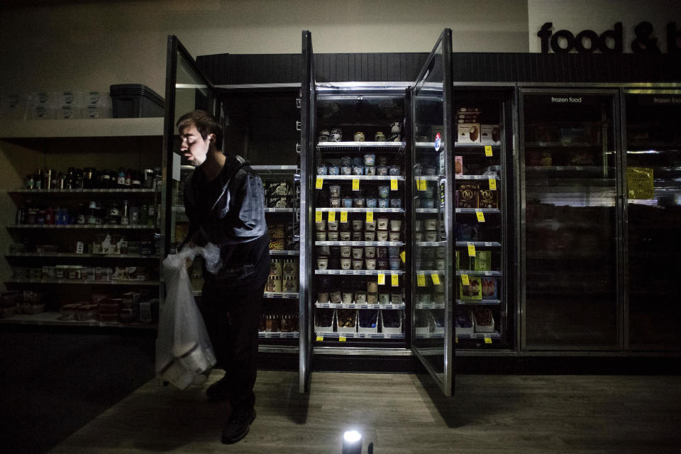 FILE - In this Oct. 9, 2019, file photo, CVS Pharmacy shift supervisor James Quinn throws out ice cream from darkened freezers as downtown Sonoma, Calif., remains without power. California's utility regulator is issuing a series of sanctions against Pacific Gas and Electric for what it calls "failures in execution" during the largest planned power shut-off in state history to avoid wildfires. (AP Photo/Noah Berger, File)