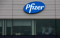 FILE -In this Wednesday, Dec. 2, 2020 file photo, two employees wave from a window at Pfizer Manufacturing in Puurs, Belgium. As soon as it dawned on the continent more than one year ago that the virus would turn into the worst pandemic in a century, the race for a vaccine was on. In securing one, once it was available, the EU could not be as nimble as such a crisis situation demanded. The EU nations got competitive prices, but it took valuable time. (AP Photo/Virginia Mayo, File