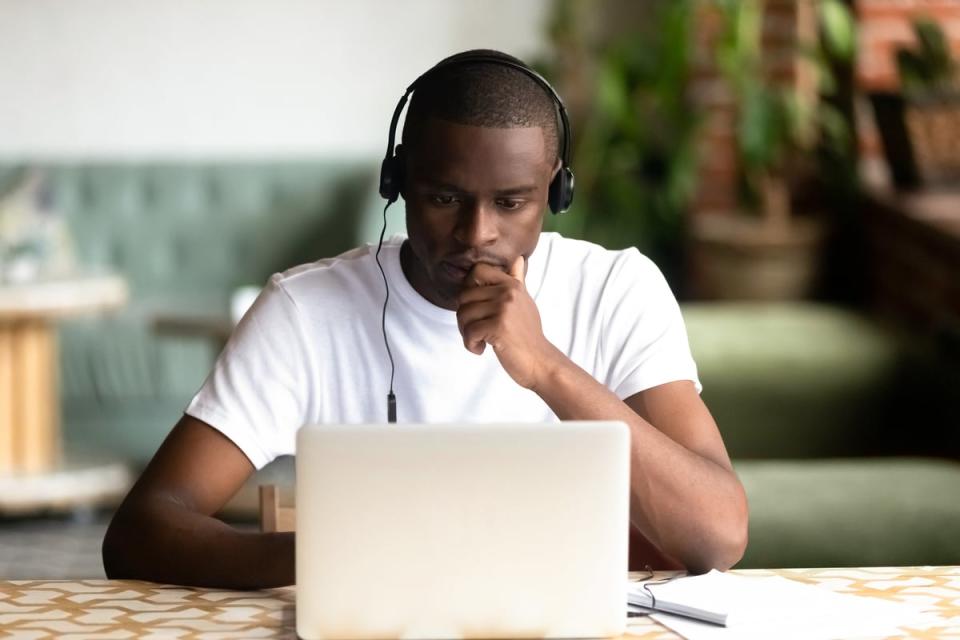 A person wearing headphones sits behind a laptop at a table. 