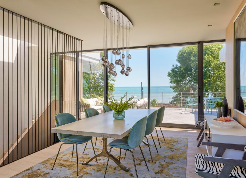 Gubi dining chairs mirror a spectacular view of Lake Michigan in a dining room by Amy Kartheiser Design. A BDDW dining table, Ochre chandelier, and Shiir rug complete the space.