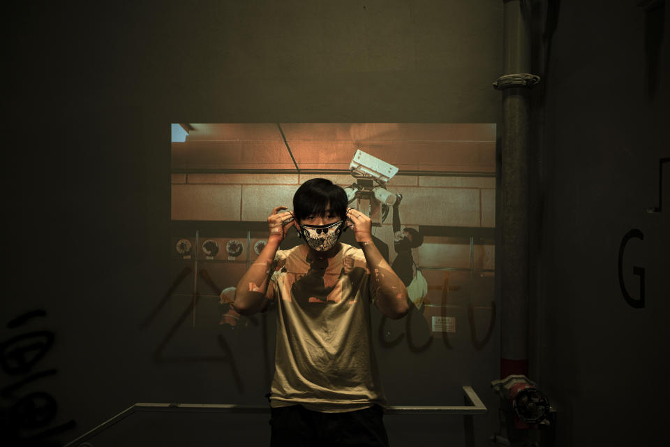 In this Oct. 16, 2019, photo, a protester who identified himself as Jason, poses for a portrait as a projector displays a photograph, previously taken during the unrest, over him at a protest in Hong Kong. In smashing, spray-painting and shining lasers on surveillance cameras across the semi-autonomous Chinese city, these demonstrators say they are fighting back against an omniscient state security apparatus that already envelops mainland China. (AP Photo/Felipe Dana)