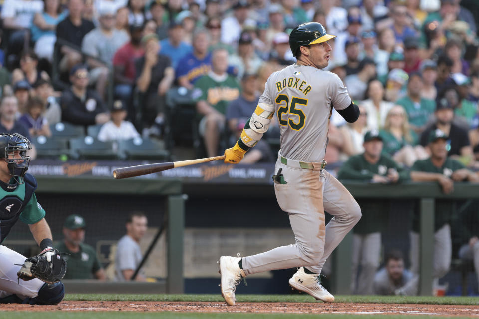 Oakland Athletics' Brent Rooker (25) follows through on an RBI single next to Seattle Mariners catcher Cal Raleigh during the third inning of a baseball game, Saturday, May 11, 2024, in Seattle. (AP Photo/Jason Redmond)