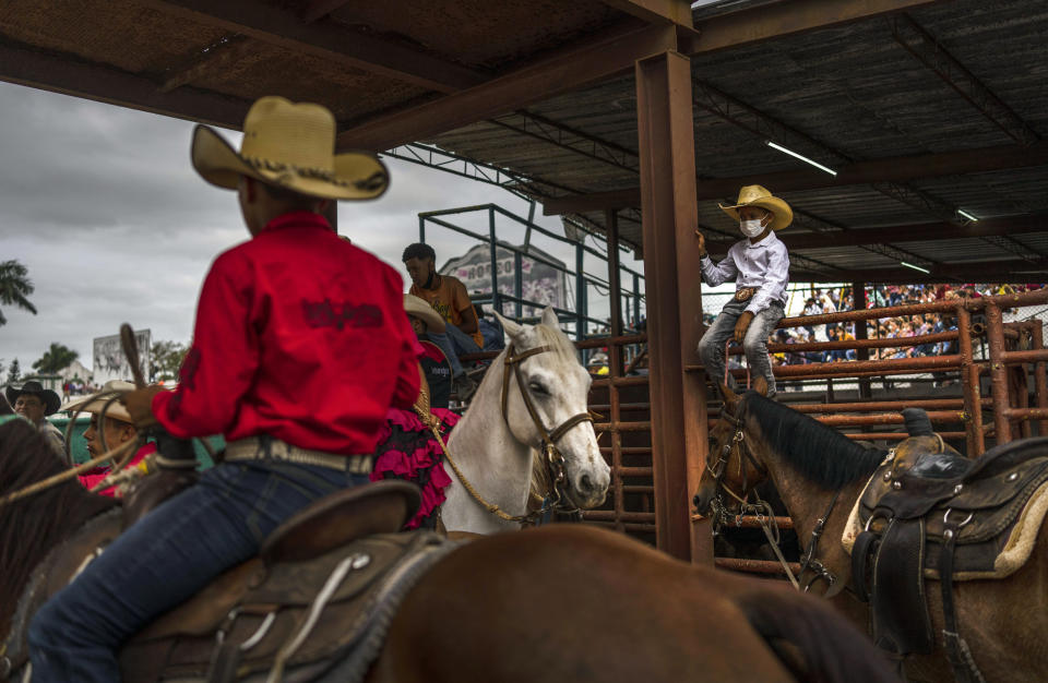 Un joven vaquero con mascarilla para prevenir la propagación del COVID-19 mira a otros competidores durante un rodeo de Ganaderos de Boyeros de la Feria Internacional Agrícola Fiagrop 2022 en La Habana, Cuba, el viernes 8 de abril de 2022. (AP Foto/Ramón Espinosa)