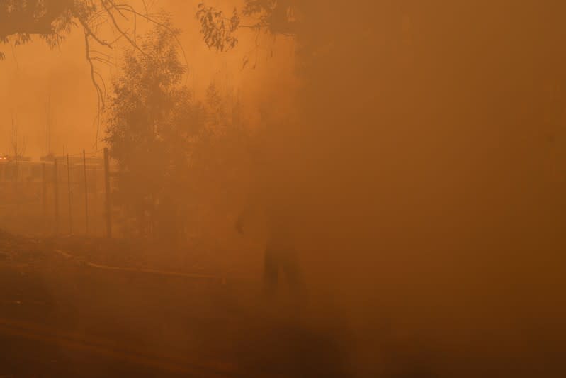 A firefighter walks in a cloud of smoke along Chalk Hill Road as he battles the wind-driven Kincade Fire in Healdsburg