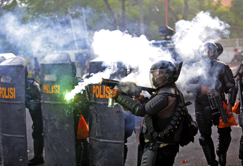 A police officer fires his tear gas launcher during a clash with student protesters in Surabaya, East Java, Indonesia, Thursday, Oct. 8, 2020. Thousands of enraged students and workers staged rallies across Indonesia on Thursday in opposition to the new law they say will cripple labor rights and harm the environment. (AP Photo/Trisnadi)