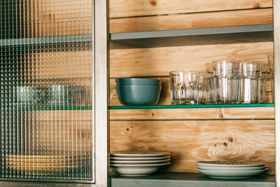 Clean plates and bowls on wooden shelf in cabinet behind glass door