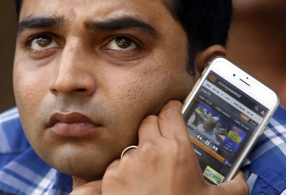 A Indian man holding a mobile phone watches a digital screen showing Indian Finance Minister Arun Jaitley presenting country’s annual budget for 2016-17 at the Parliament House in New Delhi, at the Bombay Stock Exchange in Mumbai, India, Monday, Feb. 29, 2016. India has pledged to invest billions of dollars to improve the lives of farmers and boost the rural economy, boost consumer demand and stimulate growth. Finance Minister Arun Jaitely proposed spending nearly $13 billion on rural development, promising higher incomes for farmers who form the majority of India's 1.2 billion. (AP Photo/Rajanish Kakade)