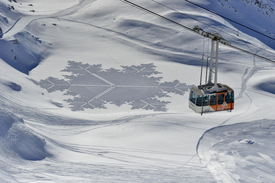 In this 2014 photo, provided by Simon Beck Snow Art, a gondola passes one of Beck's pieces in the snow at the Les Arcs ski resort in southeastern France. Using a compass, snowshoes and his background as a cartographer and competitive orienteer, the 61-year-old British artist and a handful of volunteers recently tromped across the frozen reservoir near Silverthorne, Colo., a resort town west of Denver, to create a massive, geometrical design on a fresh canvas of snow. (Simon Beck Snow Art via AP)