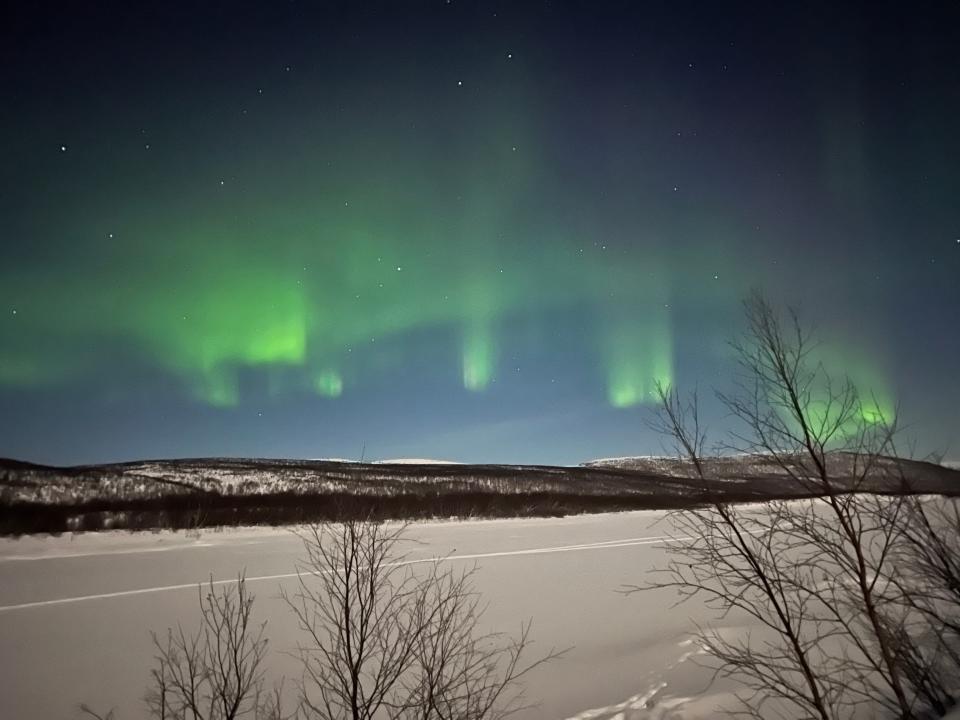 The green and purple northern lights over a snow-covered river and mountains.