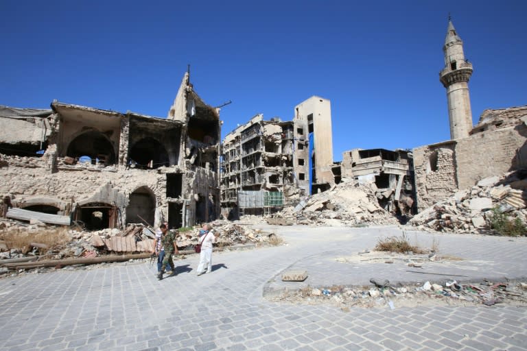 A Syrian government soldier and unidentified people walk in the damaged Khan al-Wazir market in the government-held side of Aleppo's historic city centre on September 16, 2016