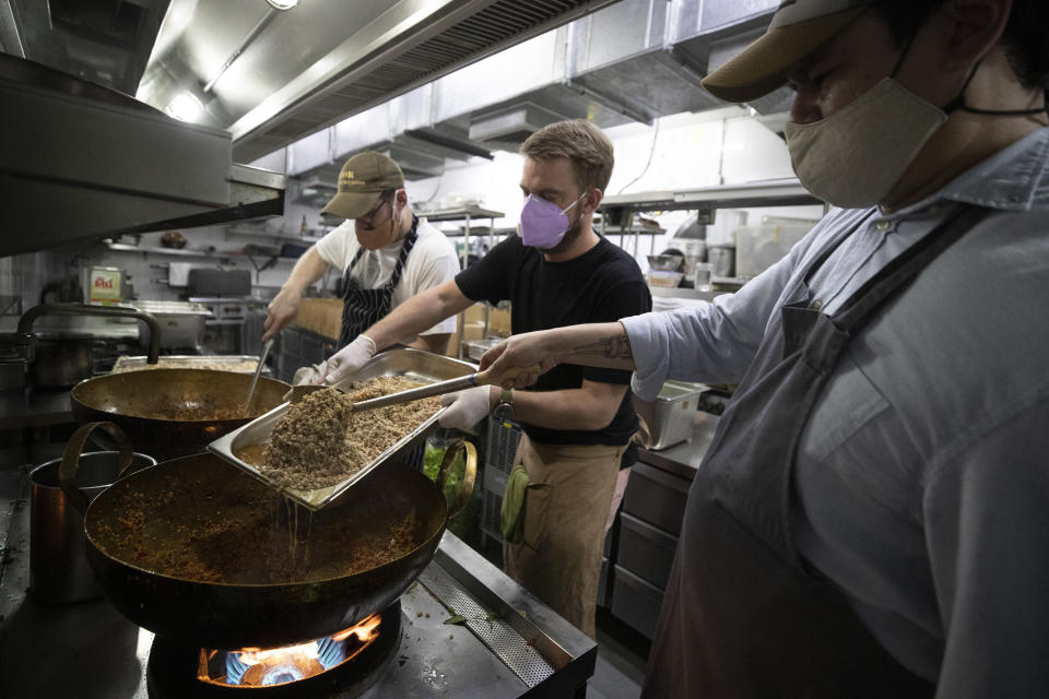 Volunteers of COVID Thailand Aid, chef Dylan Jones from Australia, left, restaurateur Jarrett Wrisley from the U.S., center, and chef Chalee Kader from Thailand cook "pad krapow gai", the spicy minced chicken for the railway-side community at Bo.lan restaurant in Bangkok, Thailand Wednesday, June 10, 2020. Thailand's Natalie Bin Narkprasert, who runs a business in Paris, was stranded in her homeland by a flight ban, so she decided to use her skills to organize a network of volunteers, including Michelin-starred chefs, to help those in her homeland whose incomes were most affected by the pandemic restrictions. (AP Photo/Sakchai Lalit)