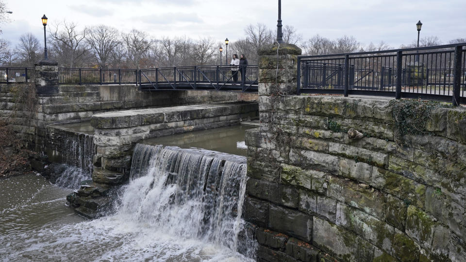 Two women look over the edge of Lower Shaker Lake Dam, Tuesday, Dec. 7, 2021, in Cleveland Heights, Ohio. In 2021, the cities of Cleveland Heights and Shaker Heights approved a $28.3 million plan to remove Horseshoe Lake Dam, return the area to a free-flowing stream and rebuild Lower Shaker Lake Dam. (AP Photo/Tony Dejak)